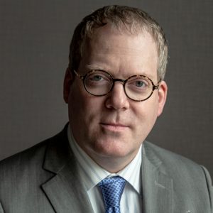 a man with glasses wearing a suit posing for a headshot
