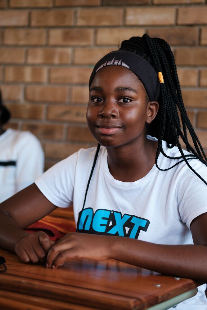 A young girl with dreadlocks sitting at a table, looking focused