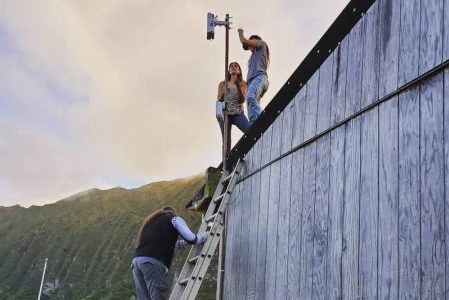 Two people on a roof of a cottage looking at the installed equipment while the third person is standing on the ladder