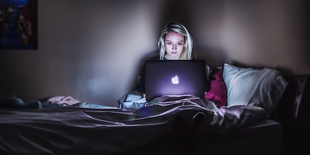 a woman sitting on the bed in dark with laptop