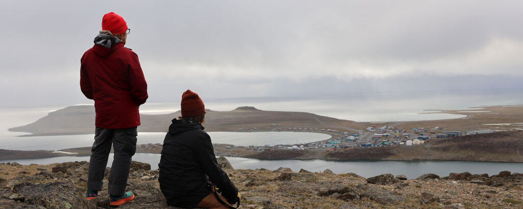 Two people on the top of a hill looking toward the horizon with a town and the ocean in the distance.