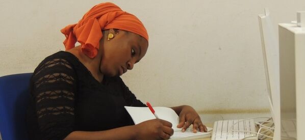 Woman in an orange turban writing on paper.