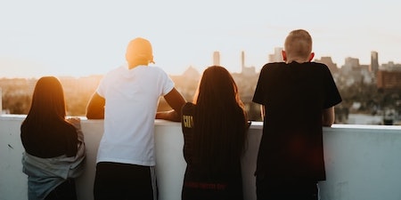 Two girls and two boys standing on the roof and watching a city in the distance